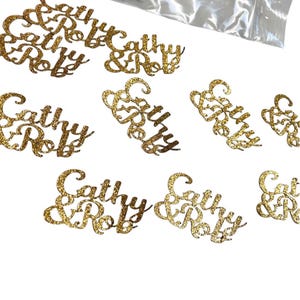 May include: Gold glitter confetti with the names "Cathy & Rob" written in a cursive font.