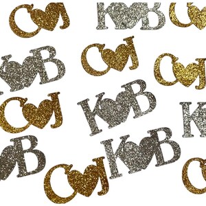 May include: Scattered glitter cutouts in gold and silver. The cutouts feature initials with a heart symbol. The initials are K, B, C, and J. The background is white.