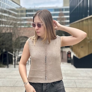 May include: A beige sleeveless knitted top with a delicate lace detail down the front. The top is cropped and has a relaxed fit.