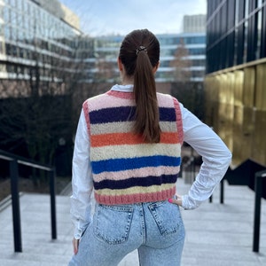 Puede incluir: Una mujer con un chaleco de punto a rayas, una camisa blanca y unos vaqueros azules.