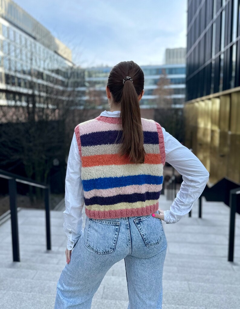 Puede incluir: Una mujer con un chaleco de punto a rayas, una camisa blanca y unos vaqueros azules.