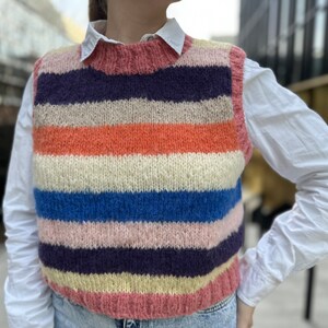 Puede incluir: Un chaleco de punto a rayas con un esquema de color rosa, naranja, azul, blanco y morado. El chaleco es sin mangas y tiene un escote redondo.