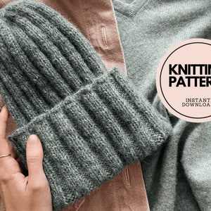 以下が含まれることがあります： リブ編み模様の緑色のニット帽。帽子は茶色と灰色の布地の背景の上に置かれています。ピンク色の円の中に「Knitting Pattern」という文字があります。