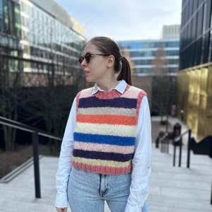 Puede incluir: Una mujer con una camisa blanca y un chaleco de punto a rayas, jeans azules y gafas de sol.