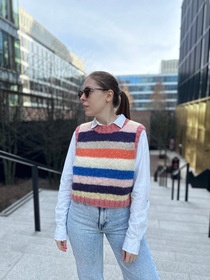 Puede incluir: Una mujer con una camisa blanca y un chaleco de punto a rayas, jeans azules y gafas de sol.