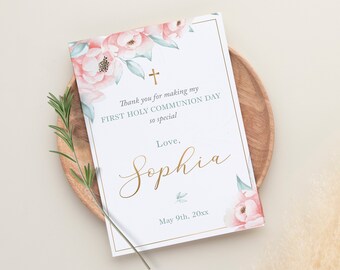 以下が含まれることがあります： 金色の縁取りとピンクの花柄が施された白いカード。カードには「私の最初の聖体拝領の日をこんなに特別にしてくれてありがとう。愛を込めて、ソフィア。20xx年5月9日」と書かれています。