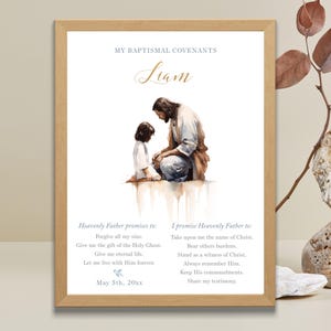Puede incluir: Una impresión enmarcada con una ilustración en acuarela de Jesús con un niño. El texto dice "Mis convenios bautismales" e incluye el nombre "Liam" en escritura dorada. La impresión también enumera promesas y una fecha.