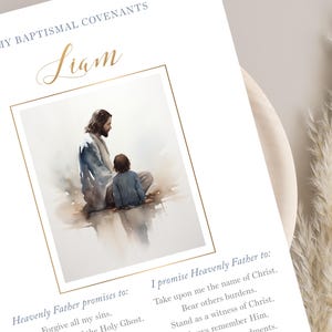 Puede incluir: Impresi&oacute;n del pacto bautismal con una ilustraci&oacute;n en acuarela de Jes&uacute;s y un ni&ntilde;o. La impresi&oacute;n incluye el nombre "Liam" en escritura dorada y texto que detalla las promesas al Padre Celestial. La combinaci&oacute;n de colores es suave y apagada.