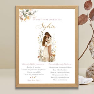 Puede incluir: Una impresión enmarcada con el texto "MY BAPTISMAL COVENANTS" y el nombre "Sophia" en escritura elegante. La impresión presenta una ilustración de dos figuras abrazándose, rodeadas de elementos florales. El texto incluye promesas y pactos.