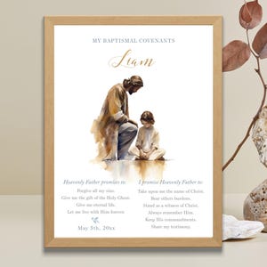 Puede incluir: Impresión enmarcada con ilustración en acuarela de una figura arrodillada ante un niño. El texto dice "Mis convenios bautismales" e incluye el nombre "Liam" en escritura dorada. La impresión también enumera promesas y convenios.