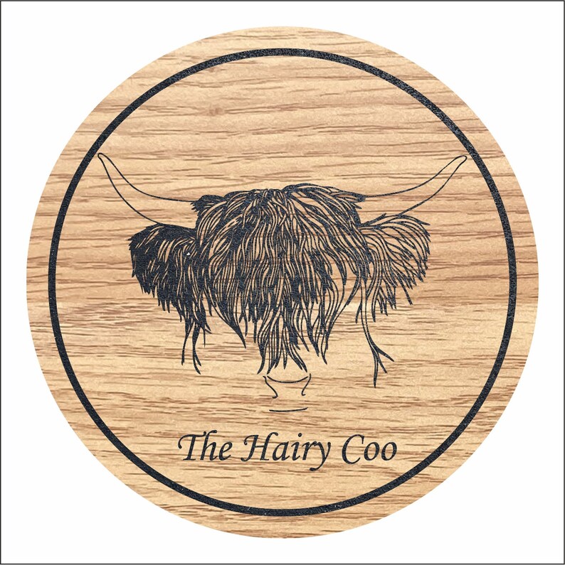 May include: A round wooden coaster featuring a black and white illustration of a Highland cow's head. The text "The Hairy Coo" is printed below the illustration.