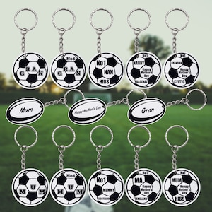 Puede incluir: Un conjunto de 10 llaveros con diseño de balón de fútbol con varios textos, incluyendo "Mum", "Gran", "No1 Nan", "No1 Nanny", "No1 Grandma", "No1 Mummy", "No1 Ma" y "No1 Mum".