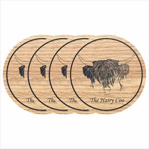 May include: Set of four round wooden coasters featuring a black and white line drawing of a Highland cow with the text "The Hairy Coo" on the bottom coaster.