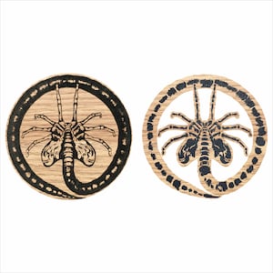 Puede incluir: Dos posavasos de madera con un gráfico en blanco y negro de una criatura extraterrestre. La criatura se representa como un gusano con cabeza y patas.
