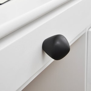 May include: A white drawer with a black, rounded knob. The drawer is open and a notebook and pen are on top of the drawer.