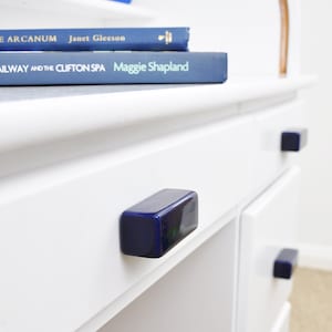 Peut inclure: Bureau blanc avec trois tiroirs et des poignées de tiroir en céramique bleue. Le tiroir supérieur a un livre intitulé "Rocks Railway and the Clifton Spa" de Maggie Shapland sur un livre intitulé "The Arcanum" de Janet Gleeson.