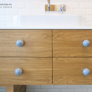 May include: A wooden bathroom vanity with four drawers and light blue round knobs. The vanity is made of light wood with a natural grain. The drawers are closed.