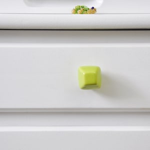 Puede incluir: Un cajón blanco con una perilla de forma geométrica verde claro.