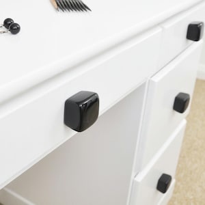 May include: White dresser with four drawers and black square drawer pulls.