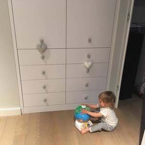 Puede incluir: Un ni&ntilde;o peque&ntilde;o juega con un juguete de globo terr&aacute;queo colorido frente a una c&oacute;moda blanca con tiradores de cajones decorativos en forma de coraz&oacute;n.