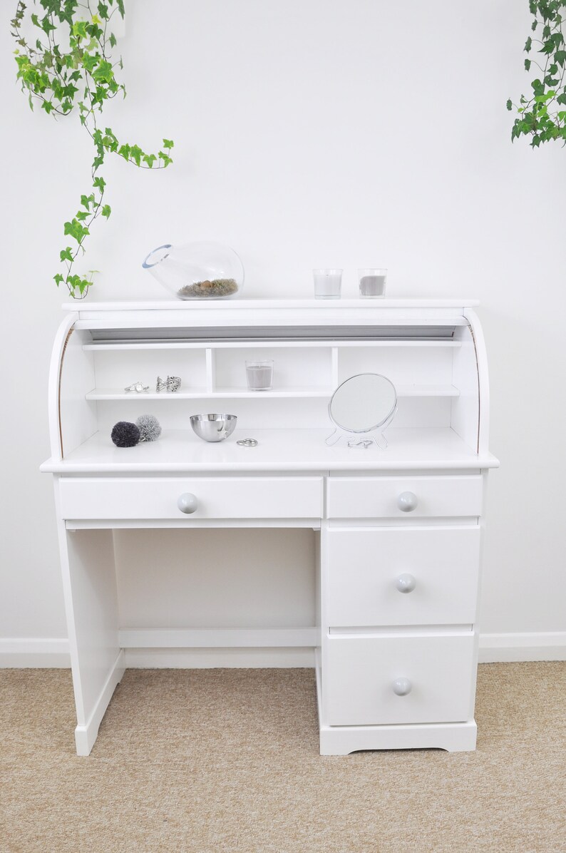 May include: White roll top desk with three drawers and a shelf above the drawers. The desk has a small round mirror and a bowl on the top surface.