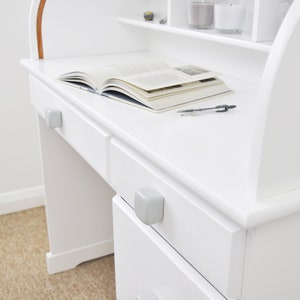 Peut inclure: Bureau en bois blanc avec un dessus incurv&eacute; et deux tiroirs. Le bureau a un livre et un stylo sur la surface. Le bureau a une finition blanche.