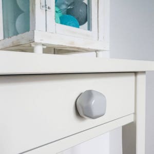 Peut inclure: Chevet blanc avec un seul tiroir et une poignée en céramique blanche. Le tiroir est fermé.