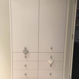 Puede incluir: Armario blanco con seis cajones a cada lado. Los cajones tienen tiradores en forma de coraz&oacute;n, algunos son grises y otros son blancos.
