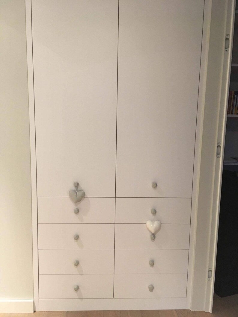 Puede incluir: Armario blanco con seis cajones a cada lado. Los cajones tienen tiradores en forma de coraz&oacute;n, algunos son grises y otros son blancos.
