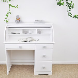 Peut inclure: Bureau blanc &agrave; roulettes avec trois tiroirs et une &eacute;tag&egrave;re au-dessus de la surface du bureau. Le bureau a une tortue en peluche grise pos&eacute;e dessus.