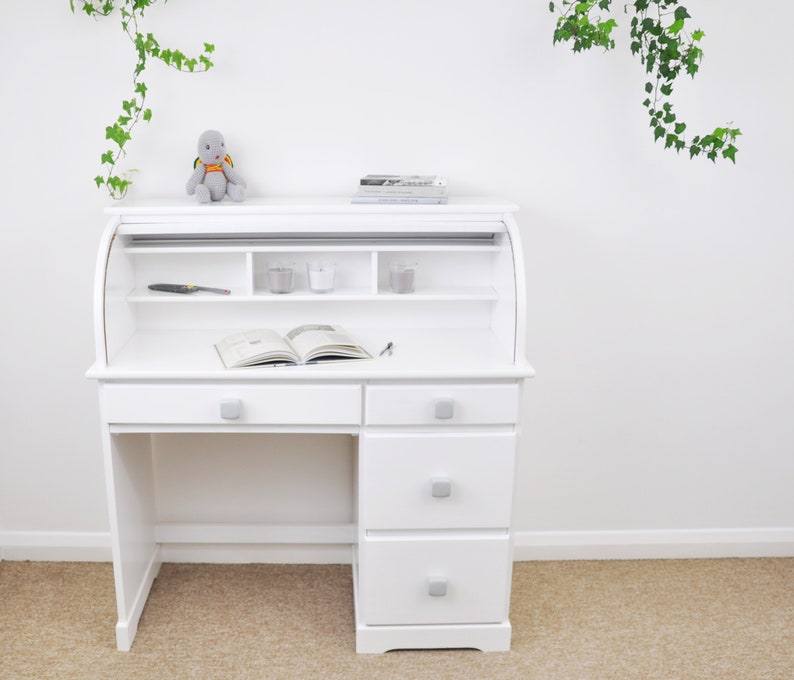 Peut inclure: Bureau blanc &agrave; roulettes avec trois tiroirs et une &eacute;tag&egrave;re au-dessus de la surface du bureau. Le bureau a une tortue en peluche grise pos&eacute;e dessus.