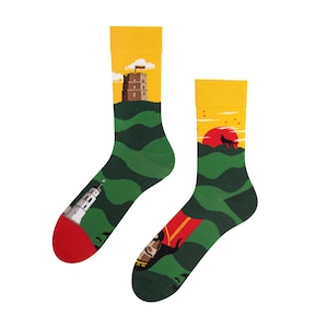 May include: A pair of colourful socks with a green, yellow and red design. One sock features a white tower on a green hill, while the other sock features a red sun, a black wolf and a person's face.