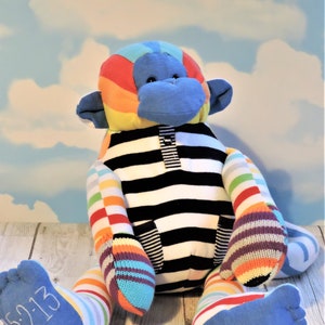 May include: A colorful stuffed monkey toy with a black and white striped shirt. The monkey has blue feet with the date "5-2-13" embroidered on one foot.