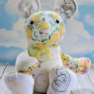 Puede incluir: Un oso de peluche de patchwork blanco y amarillo con estampado de limón. El oso tiene una cinta amarilla alrededor del cuello y las palabras "Mara" y "Mamá y Papá" están escritas en sus pies.