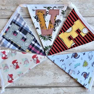 Puede incluir: Una pancarta de tela colorida con las letras "E V E" en forma de triángulo. Cada letra es de un color diferente y tiene un patrón diferente. La pancarta está hecha de diferentes telas con varios patrones, incluyendo cuadros, rayas e estampados de animales.