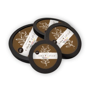 Könnte beinhalten: Vier runde, schwarz-braune Untersetzer mit weißem Blumendesign und Text. Jeder Untersetzer ist mit "Black Brown", "Echte Glas | Real Glass" und den Maßen 4-30cm und 1,57-11,8" beschriftet. Hergestellt in Deutschland.