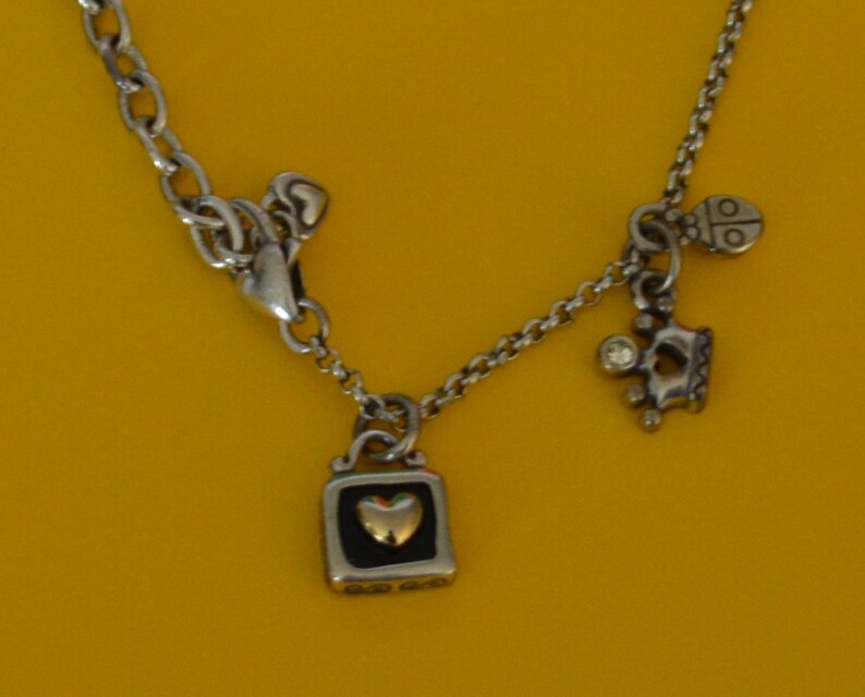 May include: A silver necklace with a heart-shaped charm, a crown charm, and a ladybug charm. The heart charm has a gold center.