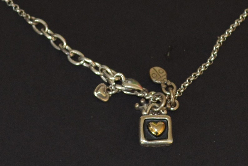 May include: A silver chain necklace with a silver charm in the shape of a television with a gold heart inside. The charm is attached to a silver chain with a silver heart charm and a silver ladybug charm.