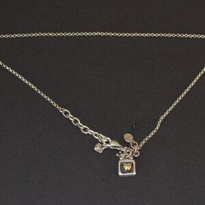 May include: A silver chain necklace with a small square pendant featuring a gold heart. The pendant has a black background and is attached to the chain with a silver clasp.