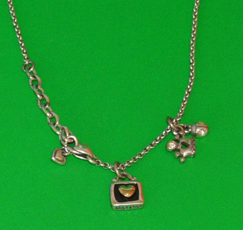 May include: A silver chain necklace with three charms: a small heart, a crown with a clear stone, and a square charm with a gold heart inside.