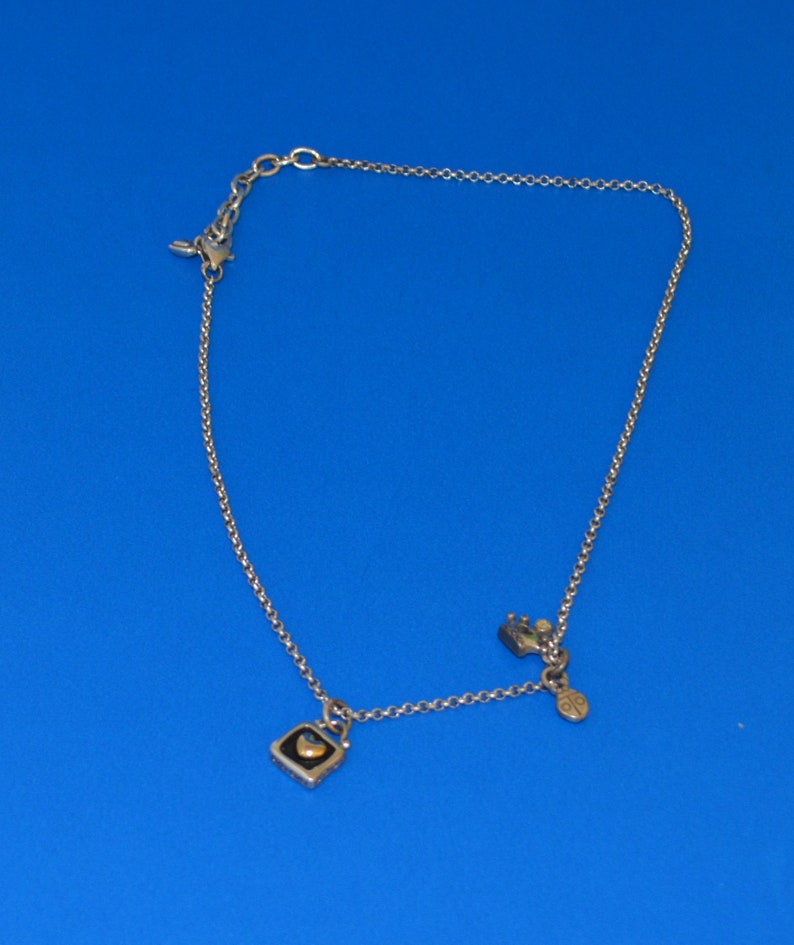 May include: A silver chain necklace with two charms. One charm is a small square with a heart inside, and the other charm is a small, round charm with a design.