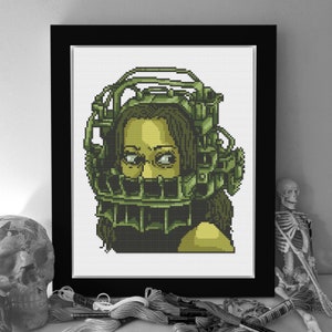 Puede incluir: Arte de punto de cruz enmarcado que presenta un retrato pixelado de una persona que lleva una jaula verde en la cabeza. La obra de arte está sobre un fondo blanco y enmarcada en negro. El tema es de terror.