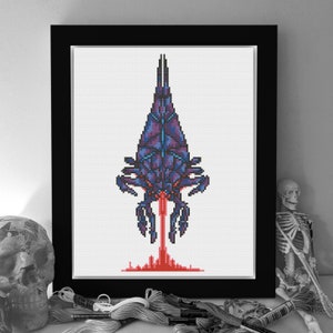 May include: Cross-stitch art framed in black. The artwork features a pixelated, geometric design of a purple and blue alien-like creature with a red beam emanating from its base. The piece is displayed on a white background.