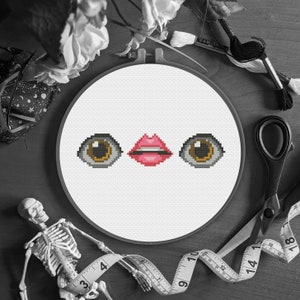 May include: A monochrome image of a cross-stitch embroidery hoop with pixelated eyes and lips. The embroidery is surrounded by sewing supplies, a skeleton, and flowers, creating a unique, artistic composition.