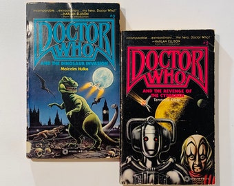 May include: Two vintage Doctor Who books. One has a blue title and features a green dinosaur with a city backdrop, titled "Doctor Who and the Dinosaur Invasion." The other has a red title and features a Cyberman, titled "Doctor Who and the Revenge of the Cybermen."