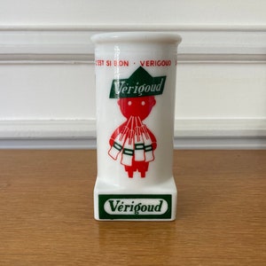 Può includere: Un contenitore in ceramica bianca con un logo verde e rosso che dice "Verigoud" e un personaggio dei cartoni animati che tiene delle bottiglie. La parte inferiore del contenitore ha il testo "Verigoud" in verde.
