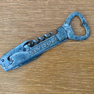 May include: A vintage metal corkscrew and bottle opener combination tool. The opener has a heart-shaped design and the word "BYRRH" is stamped on the side. The tool is silver with signs of wear.