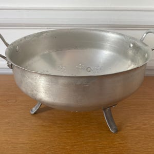 May include: A silver colander with three legs. The colander has a round bowl shape and two handles.