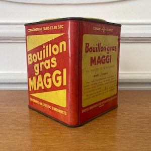 Peut inclure: Une boîte en métal vintage rouge et jaune pour Bouillon gras Maggi. La face avant porte le texte Bouillon gras MAGGI et CONTENANCE: 54 ETUIS DE 2 BATONNETS. Le côté affiche Croix Etoile, Bouillon gras MAGGI et du texte français additionnel.