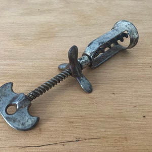 Könnte beinhalten: Ein antiker Korkenzieher aus Metall mit einem Spiraldesign und einem flügelartigen Griff. Der Korkenzieher ist aus Metall und hat eine rostige Patina.